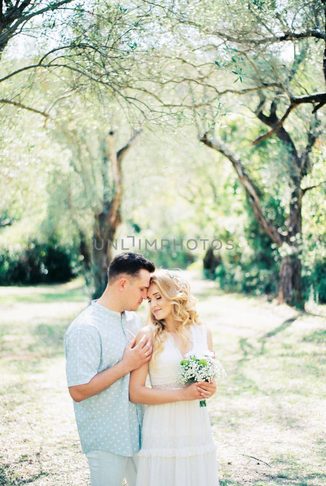 Groom hugs bride from behind with a bouquet of flowers in the park. High quality photo