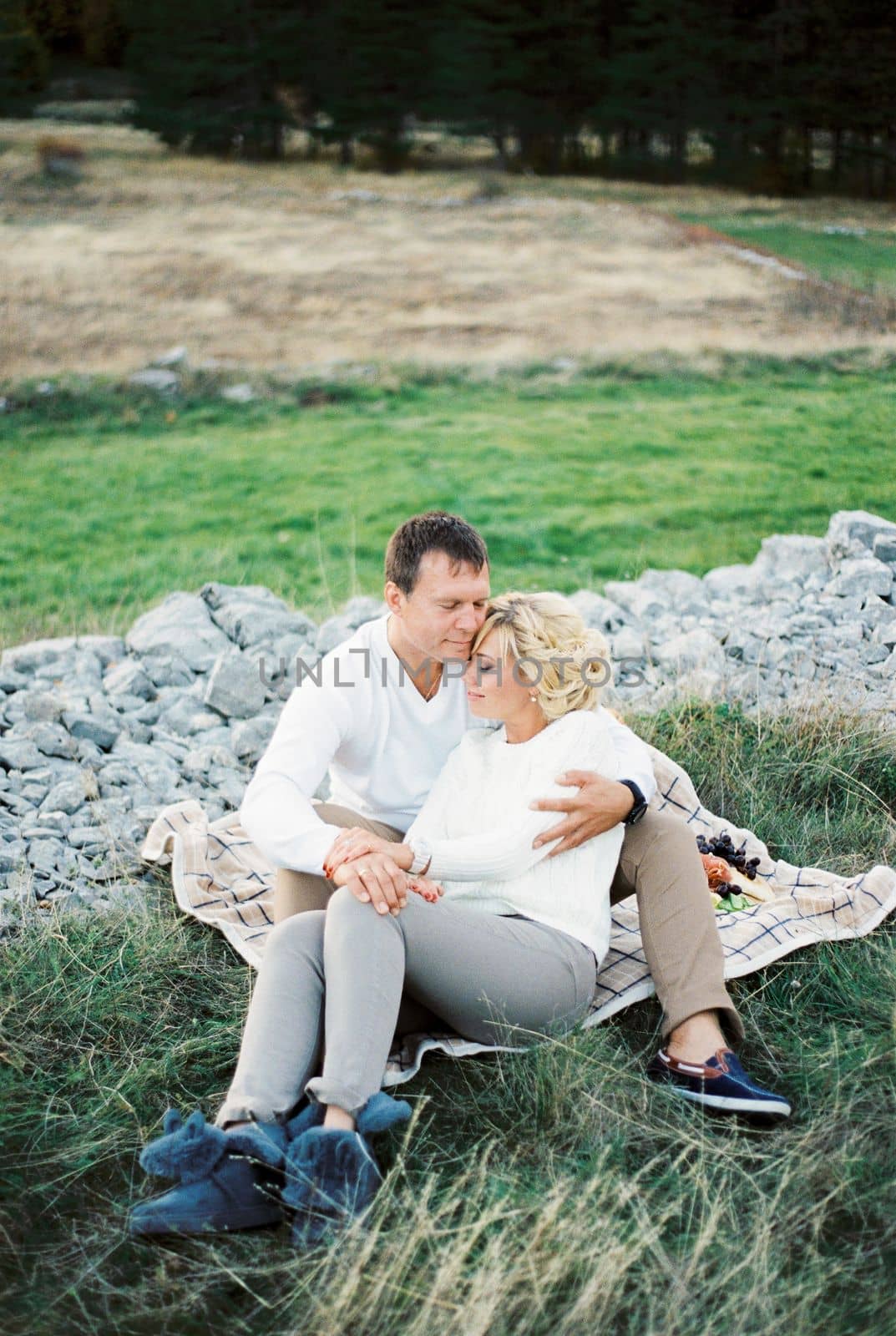 Man hugs woman leaning back against him while sitting on a blanket on the lawn. High quality photo