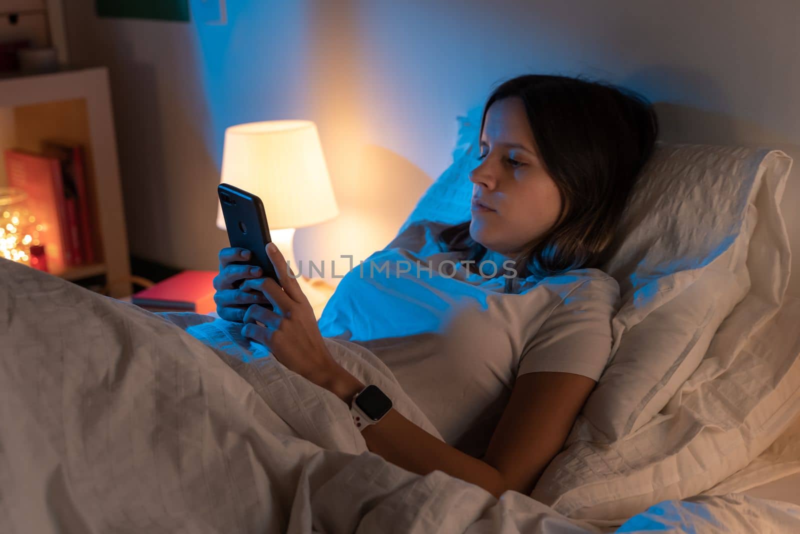 Beautiful young girl looking her phone on bed in the middle of the night. Technology at bed concept. High quality photo
