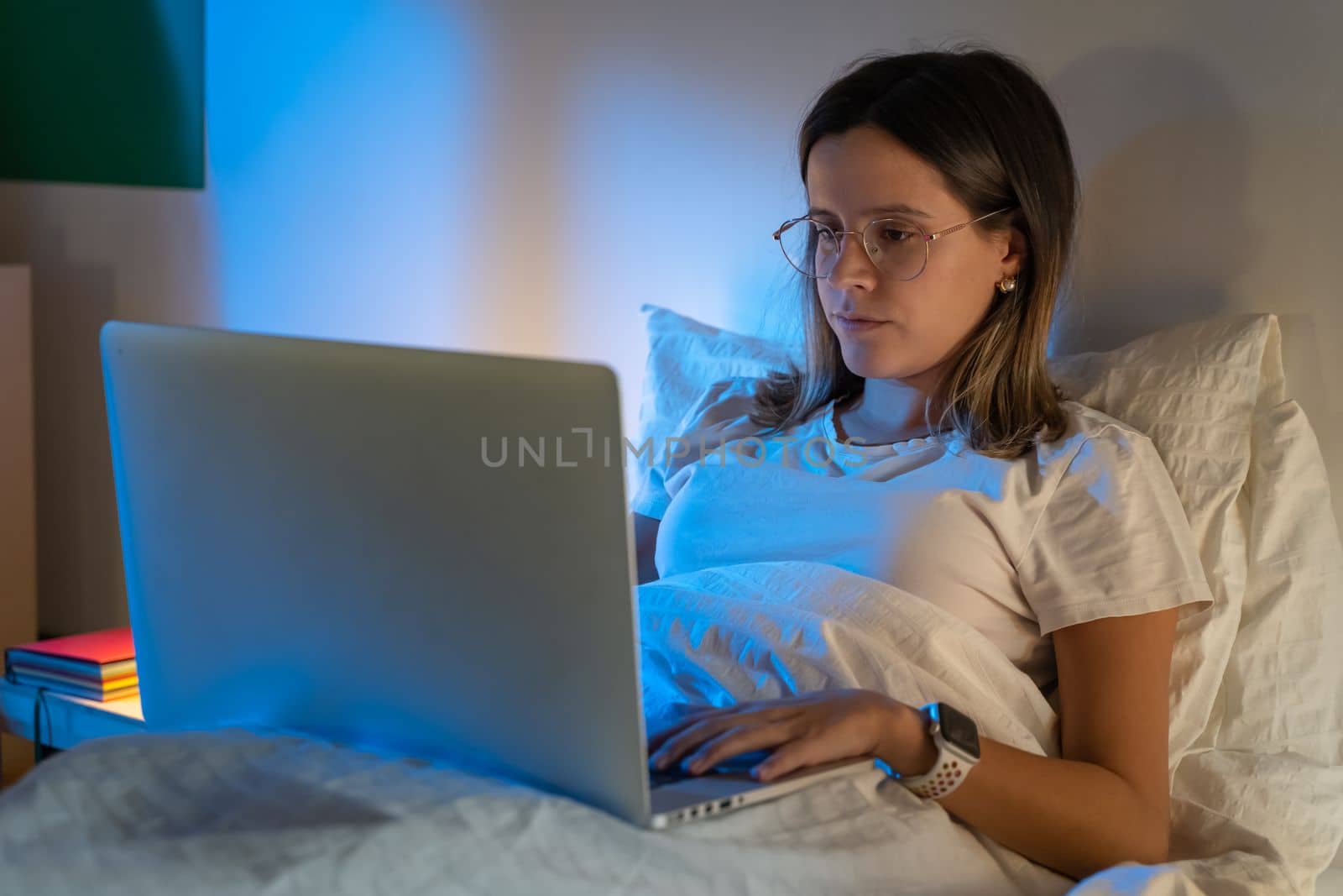 Beautiful young girl sitting on bed at night working with her laptop in the middle of the night. by PaulCarr