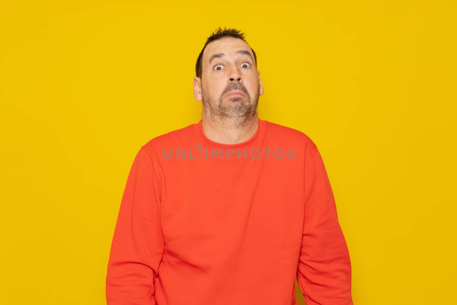 Bearded latino man wearing a red sweater with expression of doubt and confusion shrugging shoulders isolated over yellow background