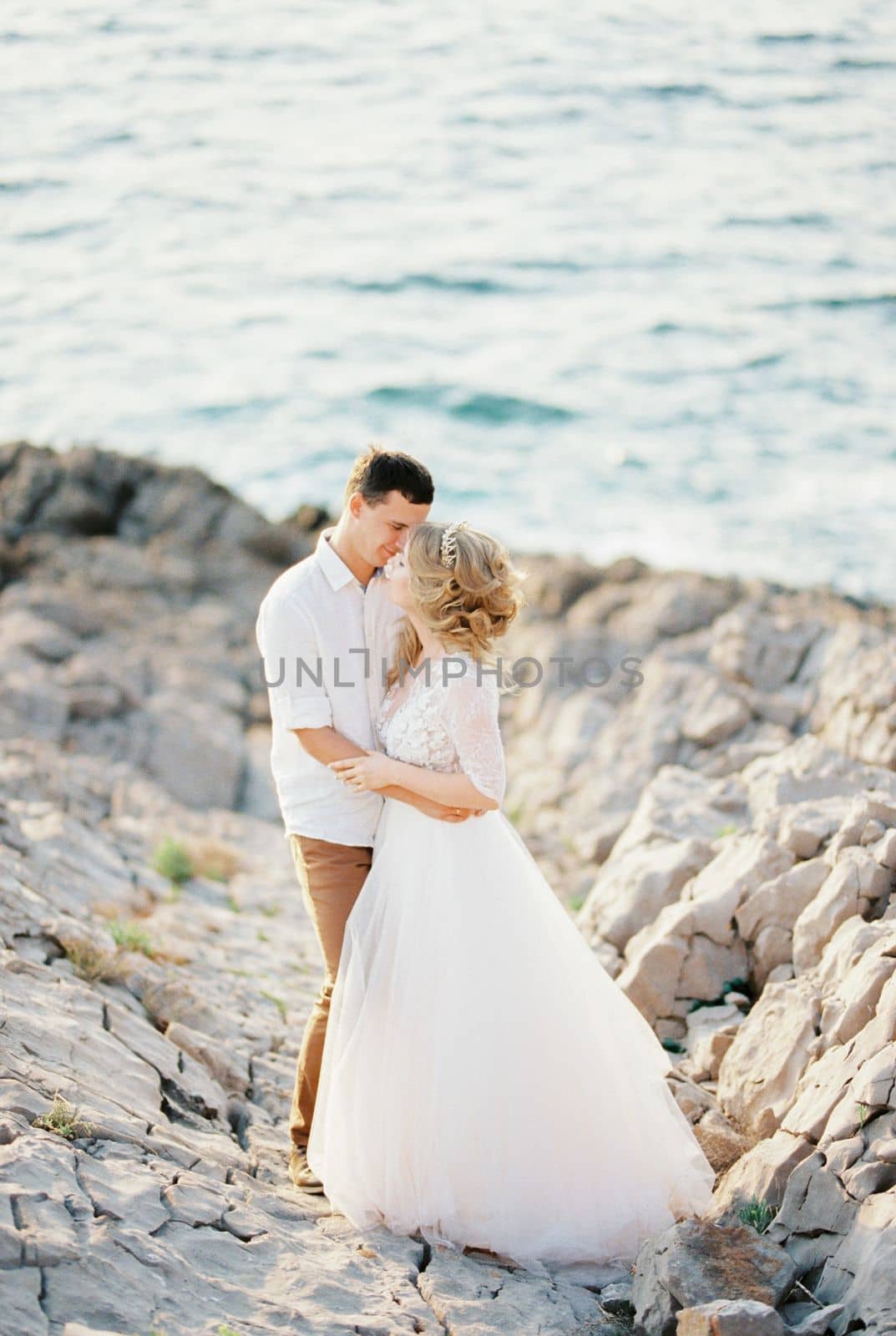 Groom hugs bride in a white lace dress on the rocks by the sea. High quality photo