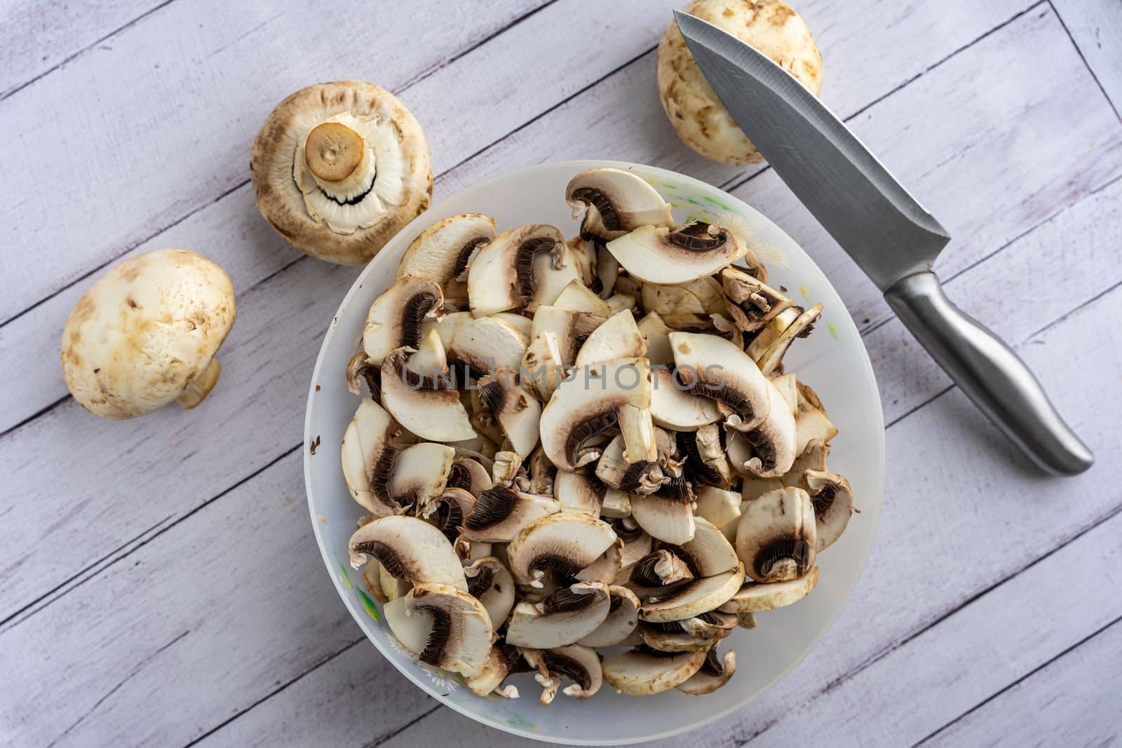 a bowl with pieces of fresh mushrooms. cut the mushrooms with a knife. Cooking mushroom dishes. Cooking dinner in the kitchen. Champignons