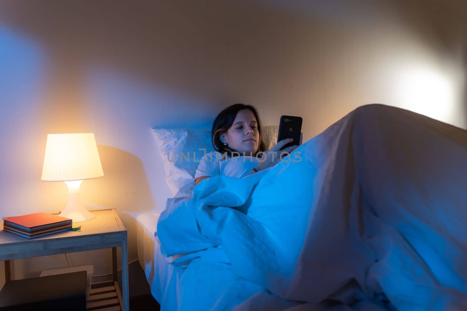 Girl looking her smart phone doom scrolling on bed in the middle of the night. Technology at bed concept. by PaulCarr