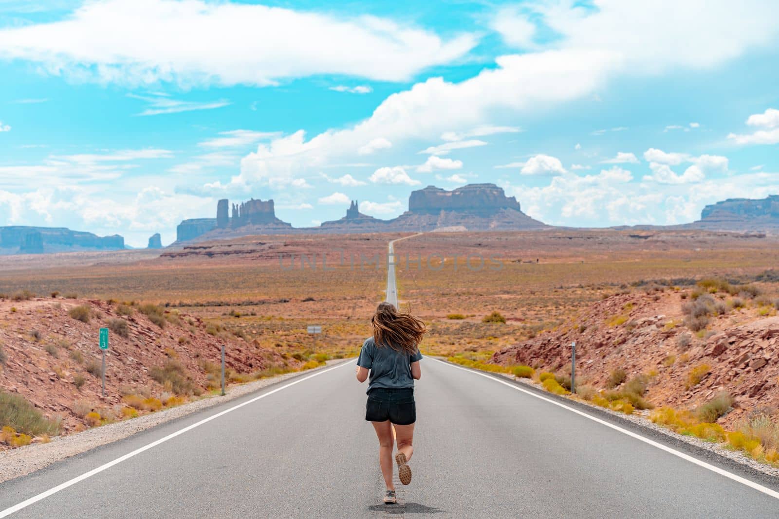 Attractive young woman from back view sitting in the middle of American straight road in the desert. High quality photo