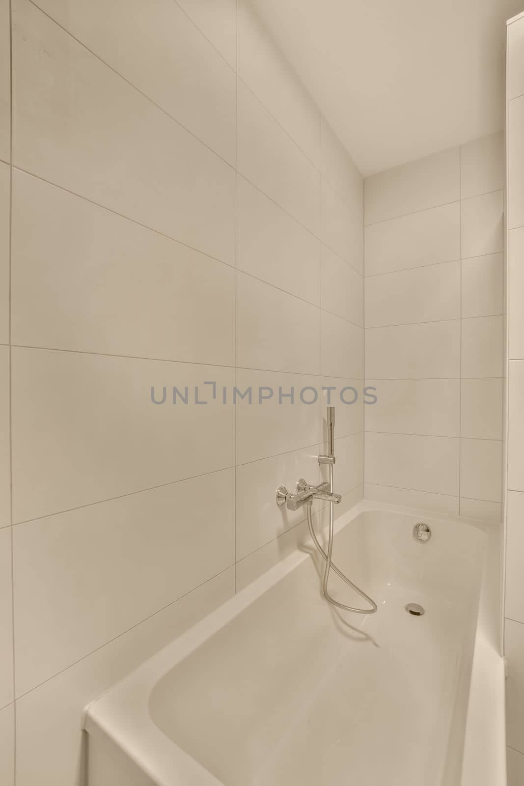a bathroom with white tiles on the walls, and a shower head in the corner of the bathtub is attached to the wall