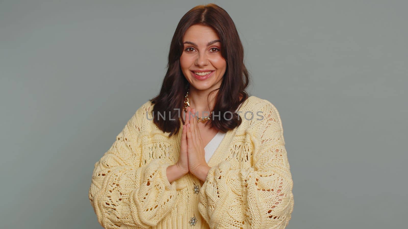 Please, God, forgive me. Young woman sincerely praying to God and looking up with pleading expression, begging apology, beseeching with hopeful face. Millennial girl isolated on gray studio background