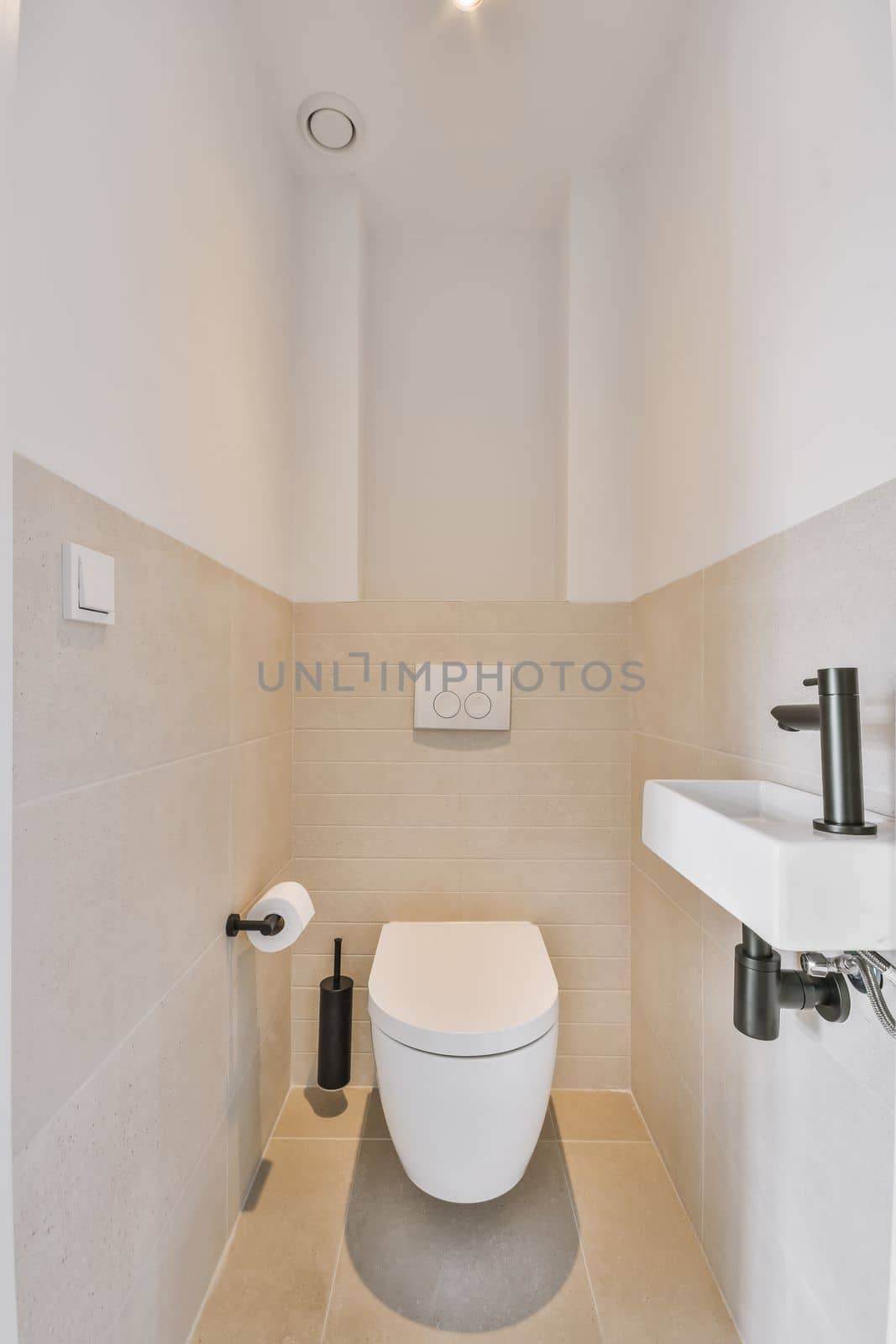 a toilet in the corner of a bathroom with beige tiles on the walls, and a white sink next to it