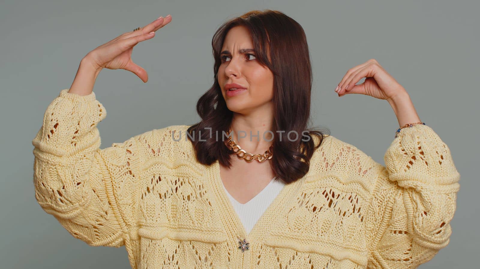 Bored pretty young woman in cardigan showing blah blah gesture with hands, has not interested in the conversation, gossips, empty promises, lier. Millennial girl isolated on gray studio background
