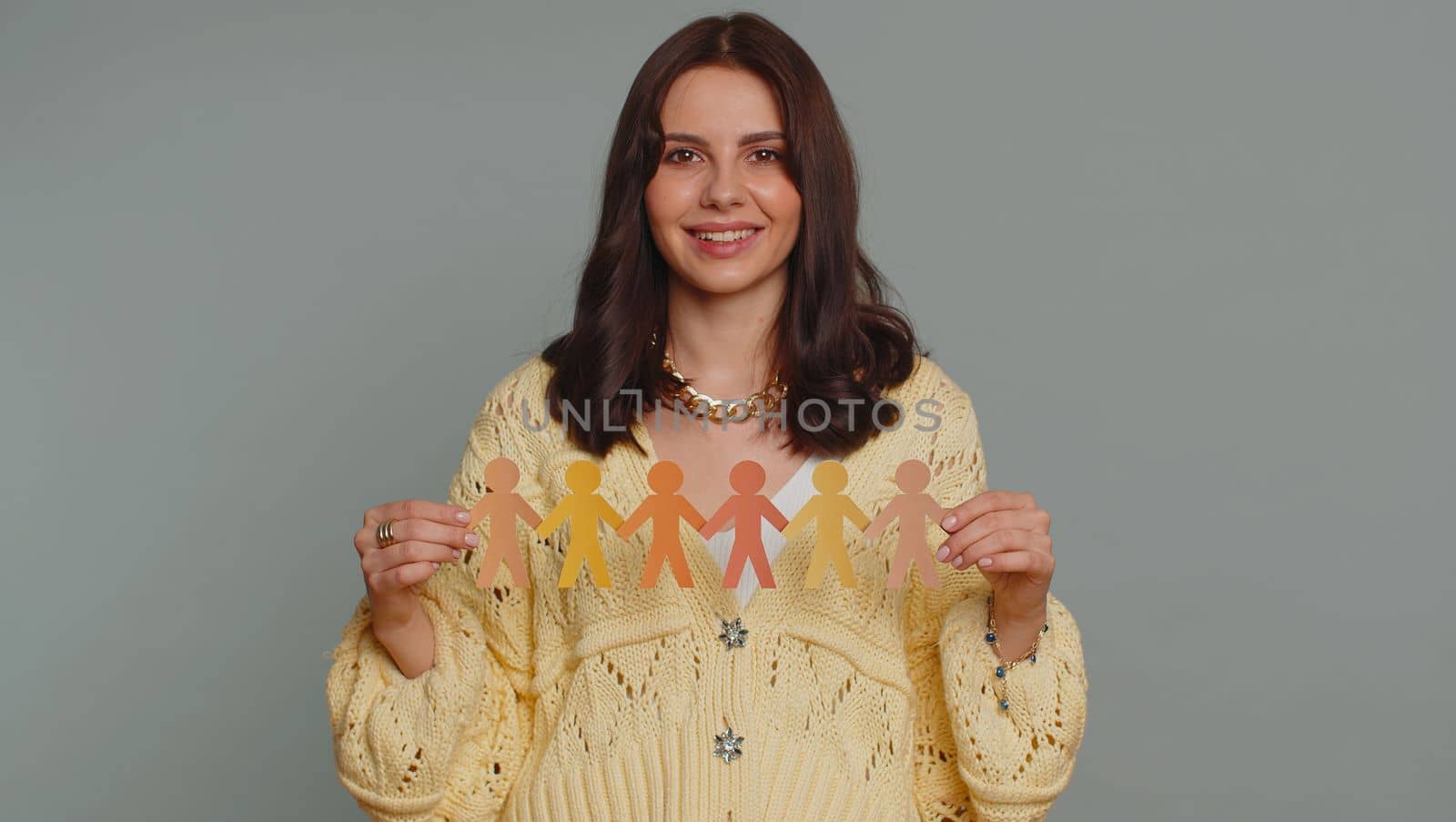Woman showing multiracial different skin color human shape cut out of paper, concept of teamwork, partnership, community, unity, people support love, against racism. Young girl on gray background
