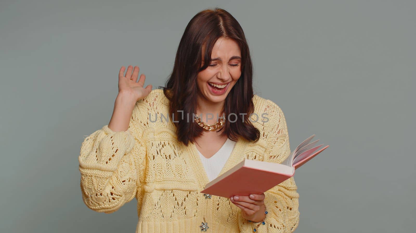 Happy pretty woman reading funny interesting fairytale story book, leisure hobby, knowledge wisdom, education, learning, study, wow. Young adult girl isolated alone on gray studio background