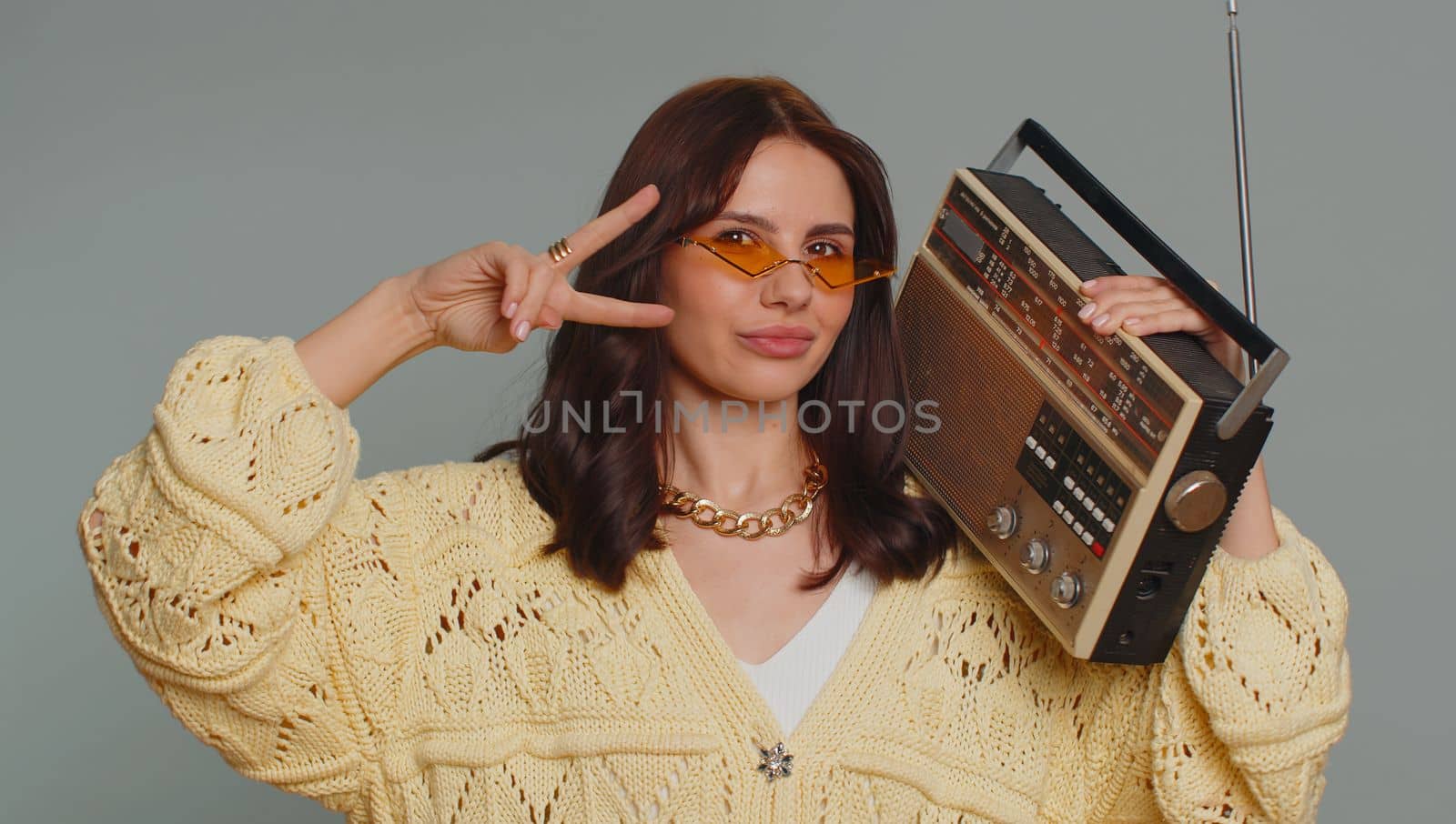 Happy woman in sunglasses using retro tape record player to listen music, disco dancing of favorite track, having fun, entertaining, fan of vintage technologies. Young girl isolated on gray background