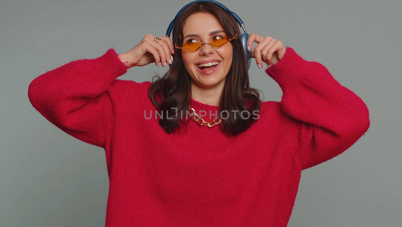 Happy pretty woman in headphones listening music and dancing disco fooling around having fun expressive gesticulating hands, relaxing on party. Caucasian girl isolated on gray studio wall background