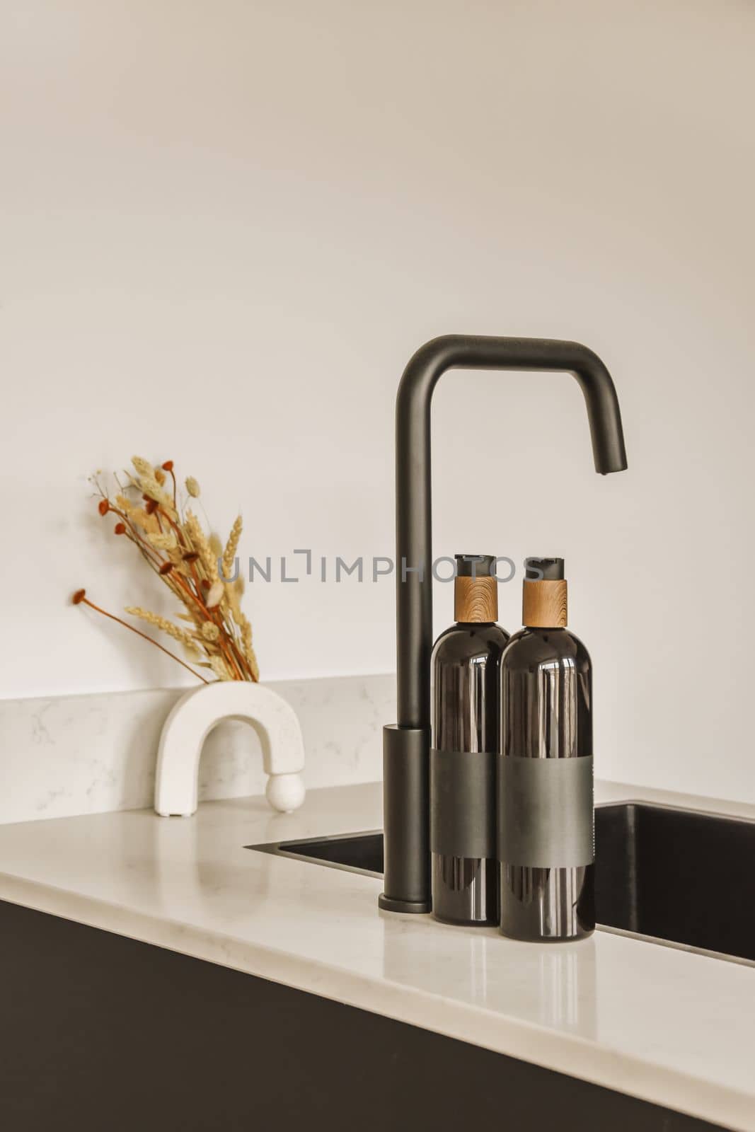 a kitchen sink with two faucets and a vase on the counter next to it in front of a white wall