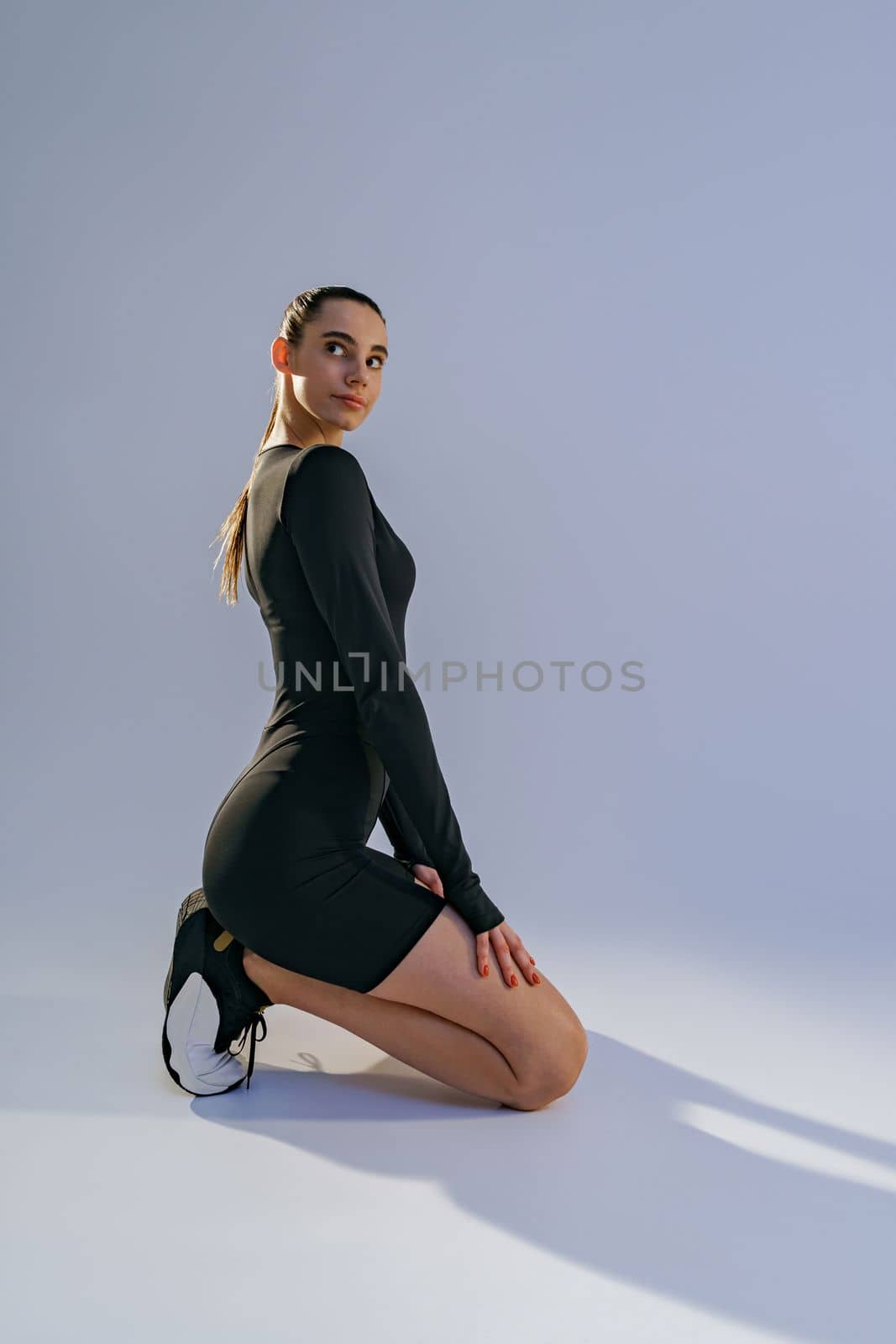 Portrait of woman wearing sportswear sitting floor on studio background and looking at camera by Yaroslav_astakhov