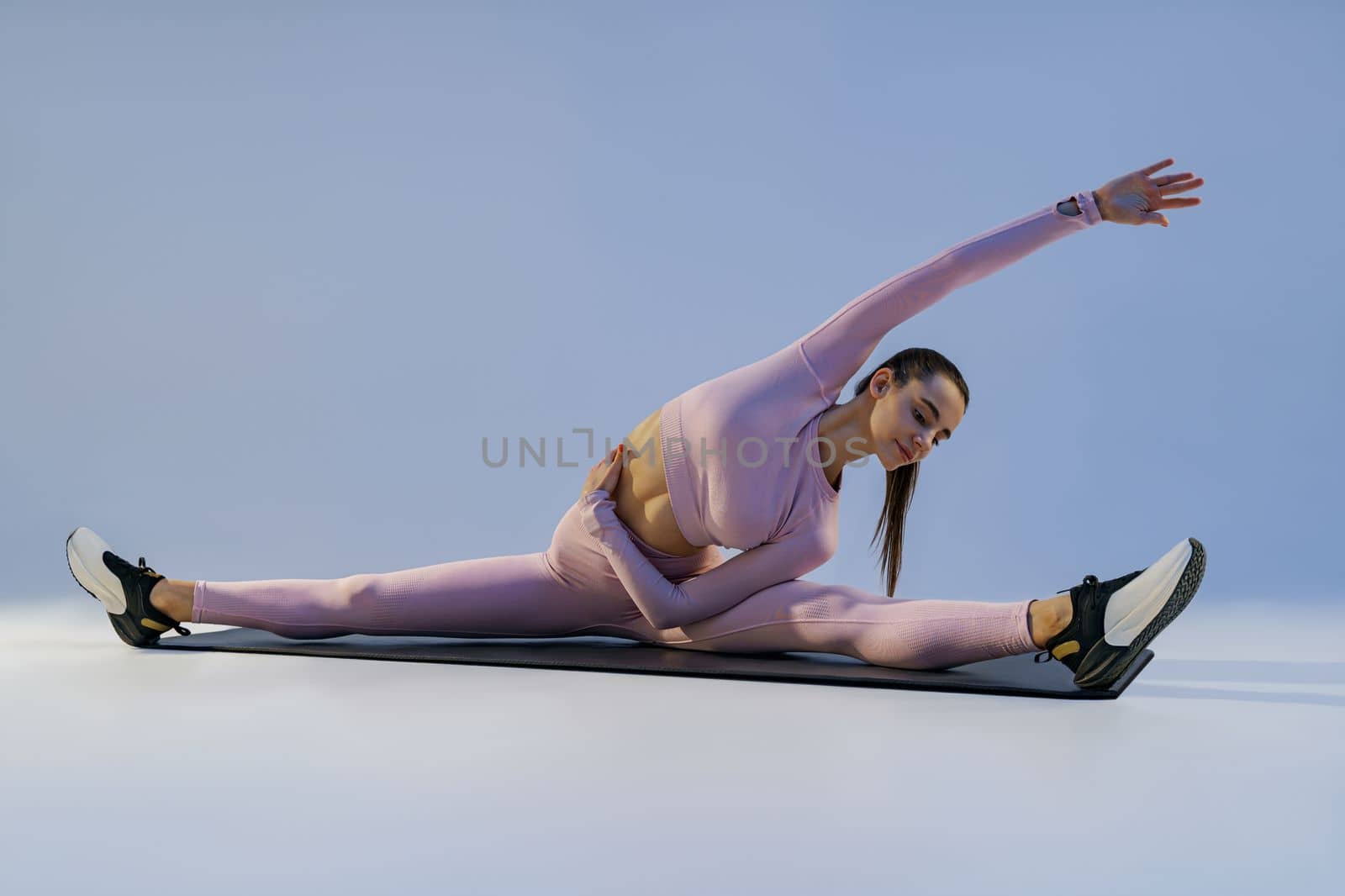 Athletic woman in sportswear doing stretching exercises on yoga mat on studio background
