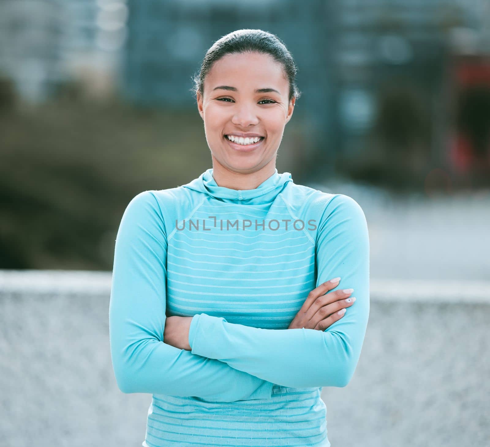 Portrait of one confident young mixed race woman standing with arms crossed ready for exercise outdoors. Determined female athlete looking happy and motivated for training workout in the city.