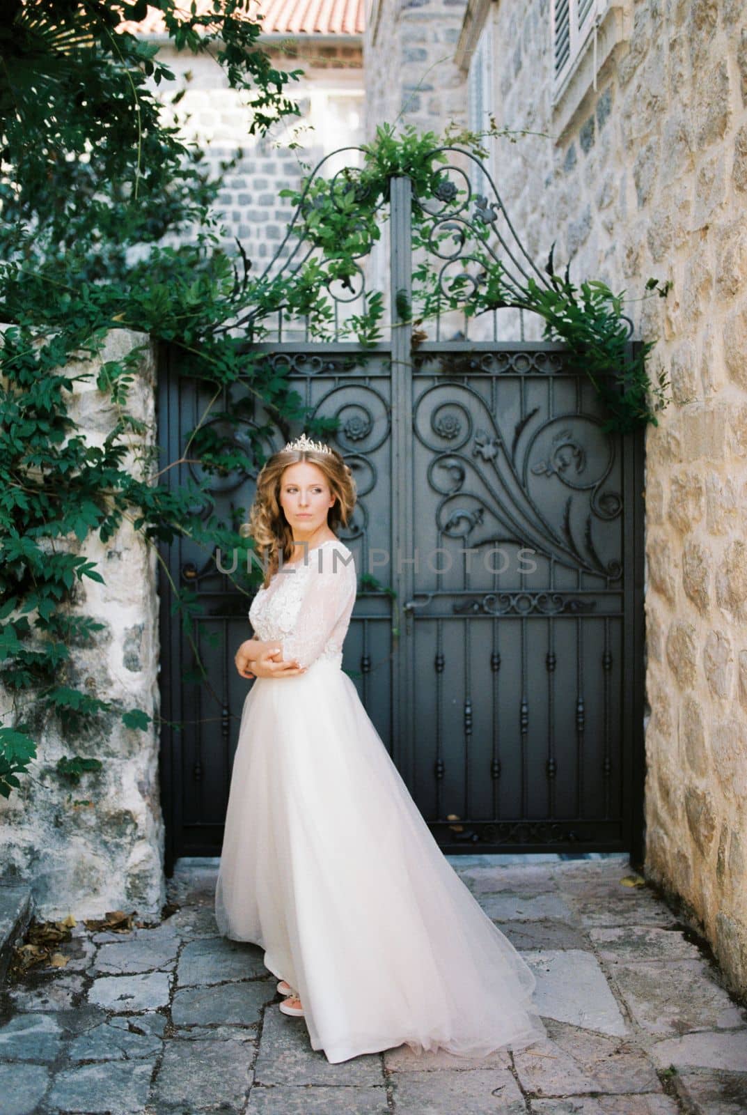 Bride in a white dress with a diadem stands in the courtyard of an old stone house. High quality photo