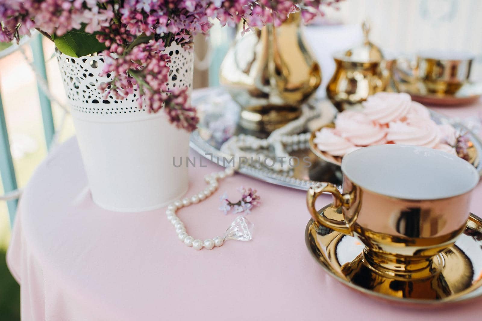 Delicate morning tea table setting with lilac flowers, antique spoons and dishes on a table with a pink tablecloth.