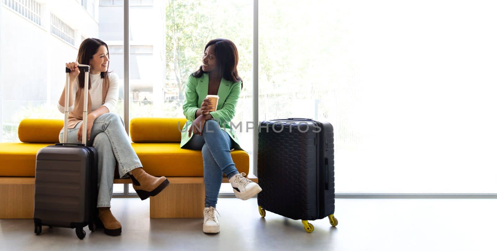 Horizontal banner image of multiracial women sitting on hotel reception bench talking. Copy space. Lifestyle and travel concept.
