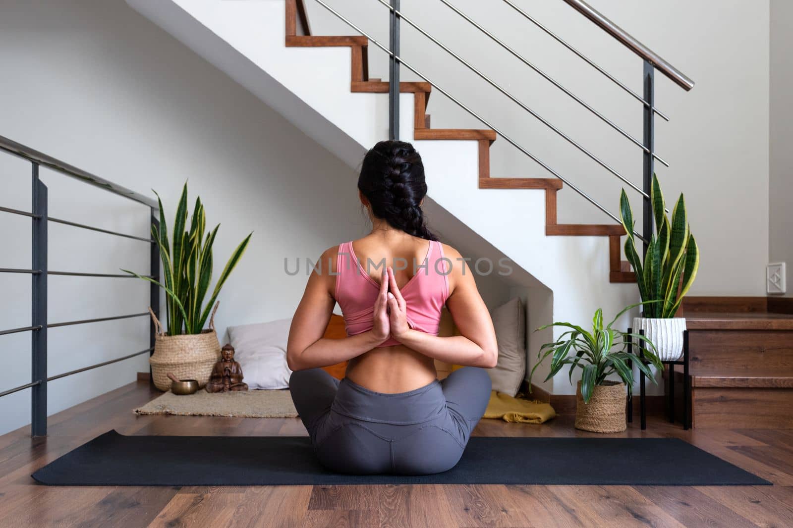 Rear view of young woman doing reverse prayer yoga pose at home living room. Female yogi doing namaste mudra behind back. Lifestyle and spirituality concept.