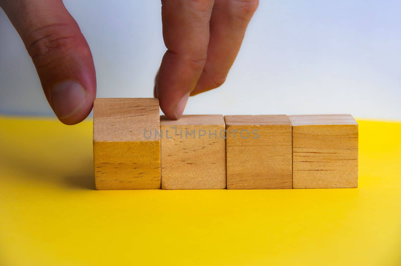 Hand turning wooden cube on yellow background. Customizable space on wooden cubes for text. Copy space.