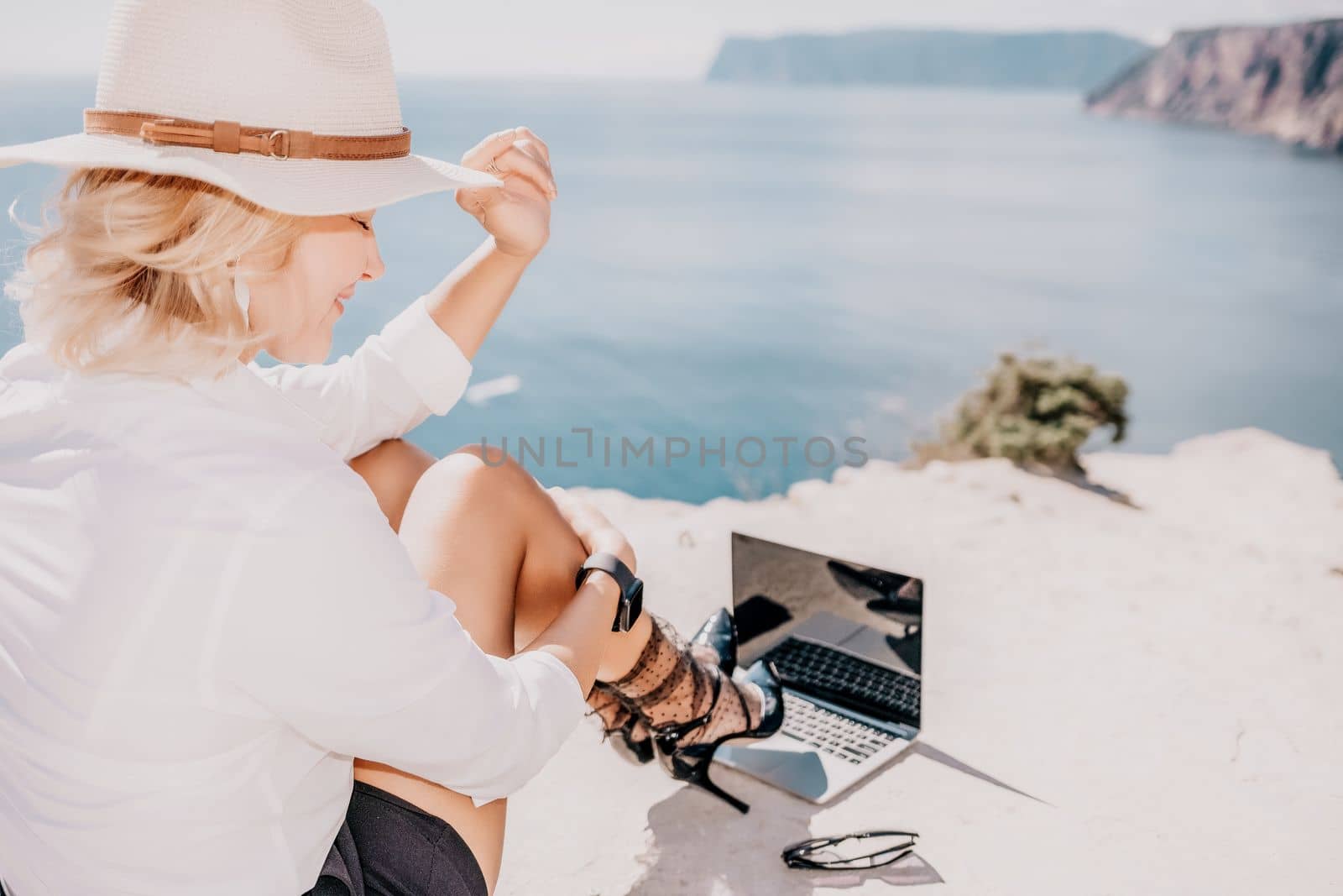 Woman sea laptop. Business woman in yellow hat freelancer with laptop working over blue sea beach. Girl relieves stress from work. Freelance, digital nomad, travel and holidays concept by panophotograph