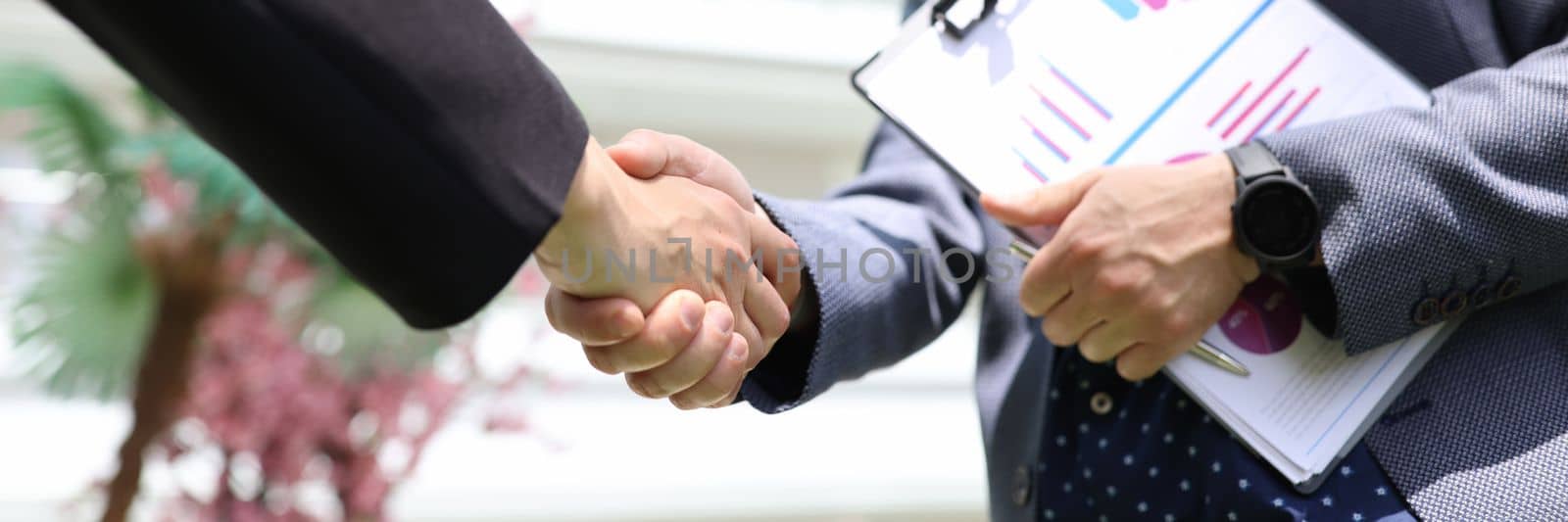 Handshake of businessmen with financial analytics charts. Business etiquette congratulations and merger and acquisition concept