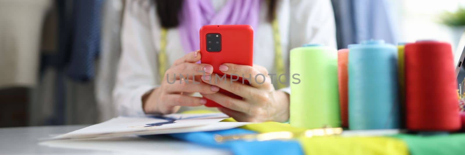 Beautiful fashion designer is sitting at table and typing on smartphone by kuprevich