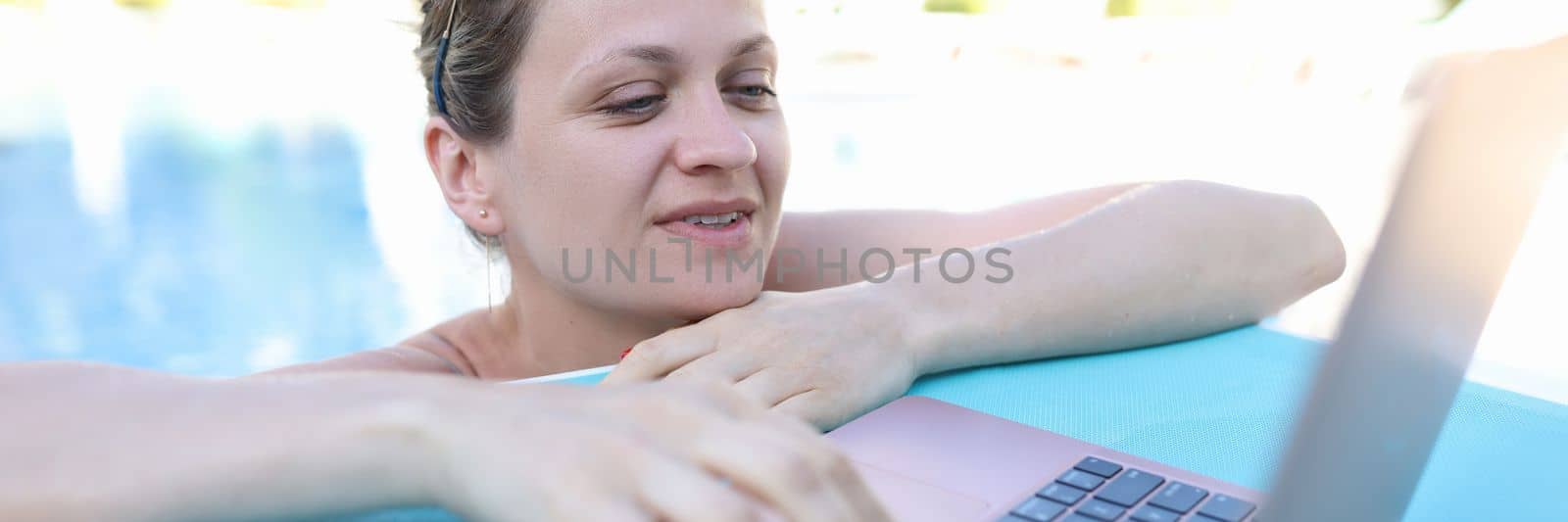Beautiful woman in pool is typing on laptop. Telework remote work and communication with subscribers