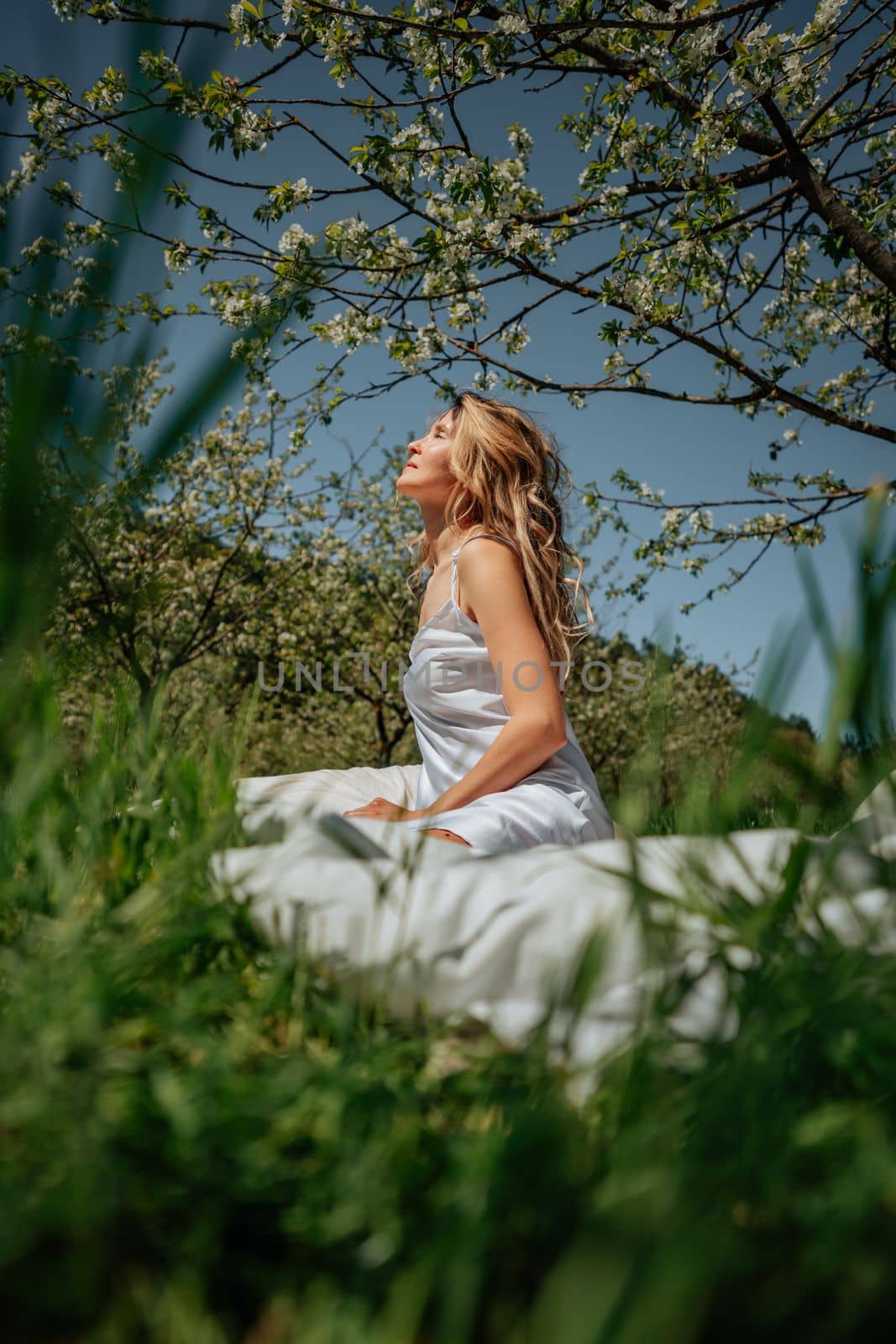 woman sleeps on a white bed in the fresh spring grass in the garden. Dressed in a blue nightgown