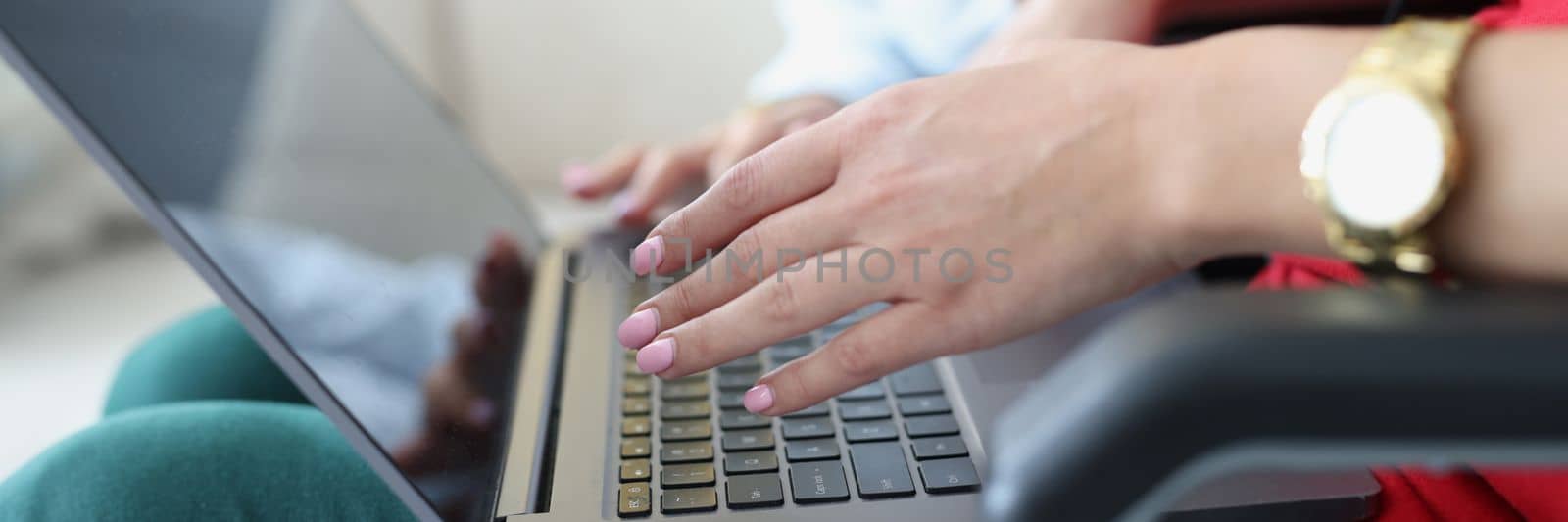 Closeup of hands of busy young woman and freelancer student friend sitting in chair with laptop. Woman typing email on computer keyboard, working at home