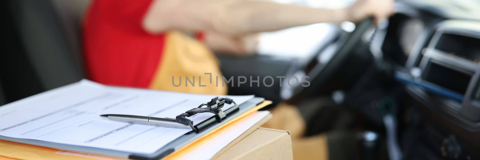 Courier in uniform in car and receipt documents on clipboard for client. Parcel delivery and courier driver services