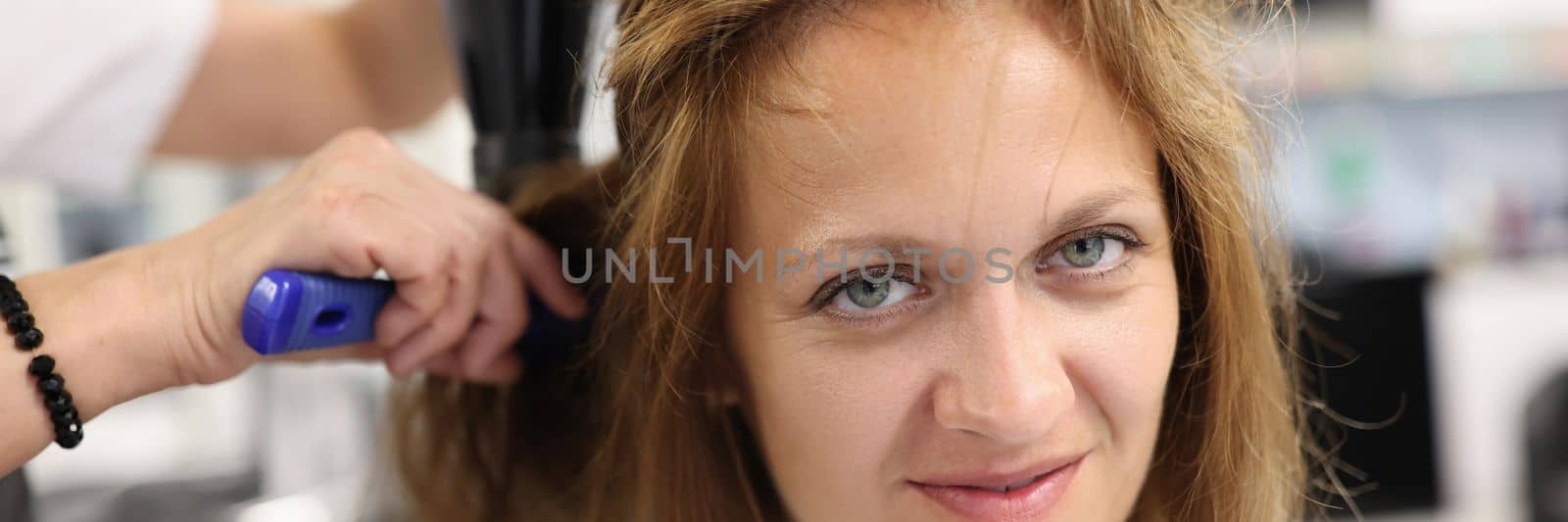 Woman hairdresser dries and straightens client hair with comb and hair dryer in beauty salon by kuprevich