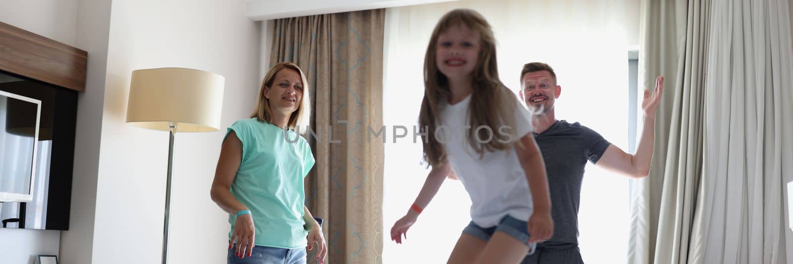 Happy family mother father and child laughing play and jump in bed in bedroom at home or hotel. Family emotions love and joy