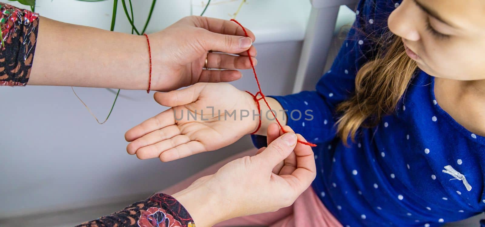 The mother ties a red thread to the child hand. Selective focus. Kid.
