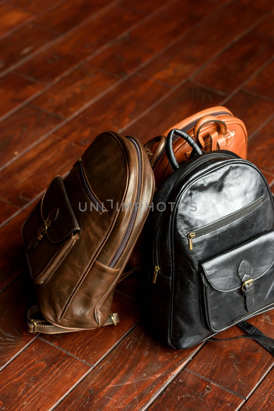 three different colored leather backpacks on a wooden floor. Indoor photo