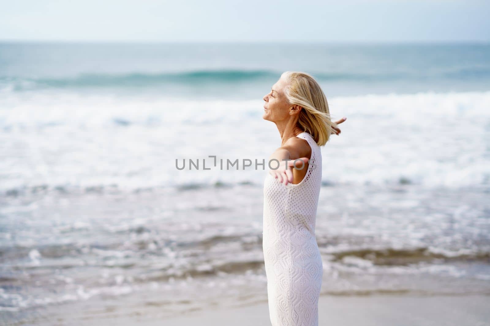 Mature woman opening her arms on a tropical beach, spending her leisure time. Elderly female enjoying her retirement at a seaside retreat.