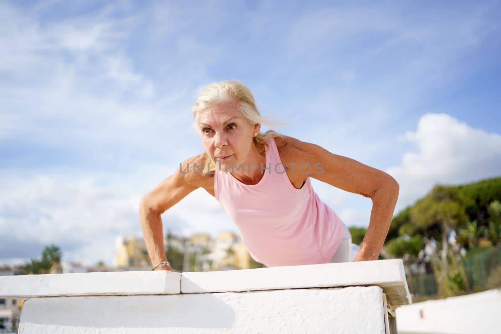 Push ups or press ups exercise by mature woman. Senior female working strength training against sky with copyspace.