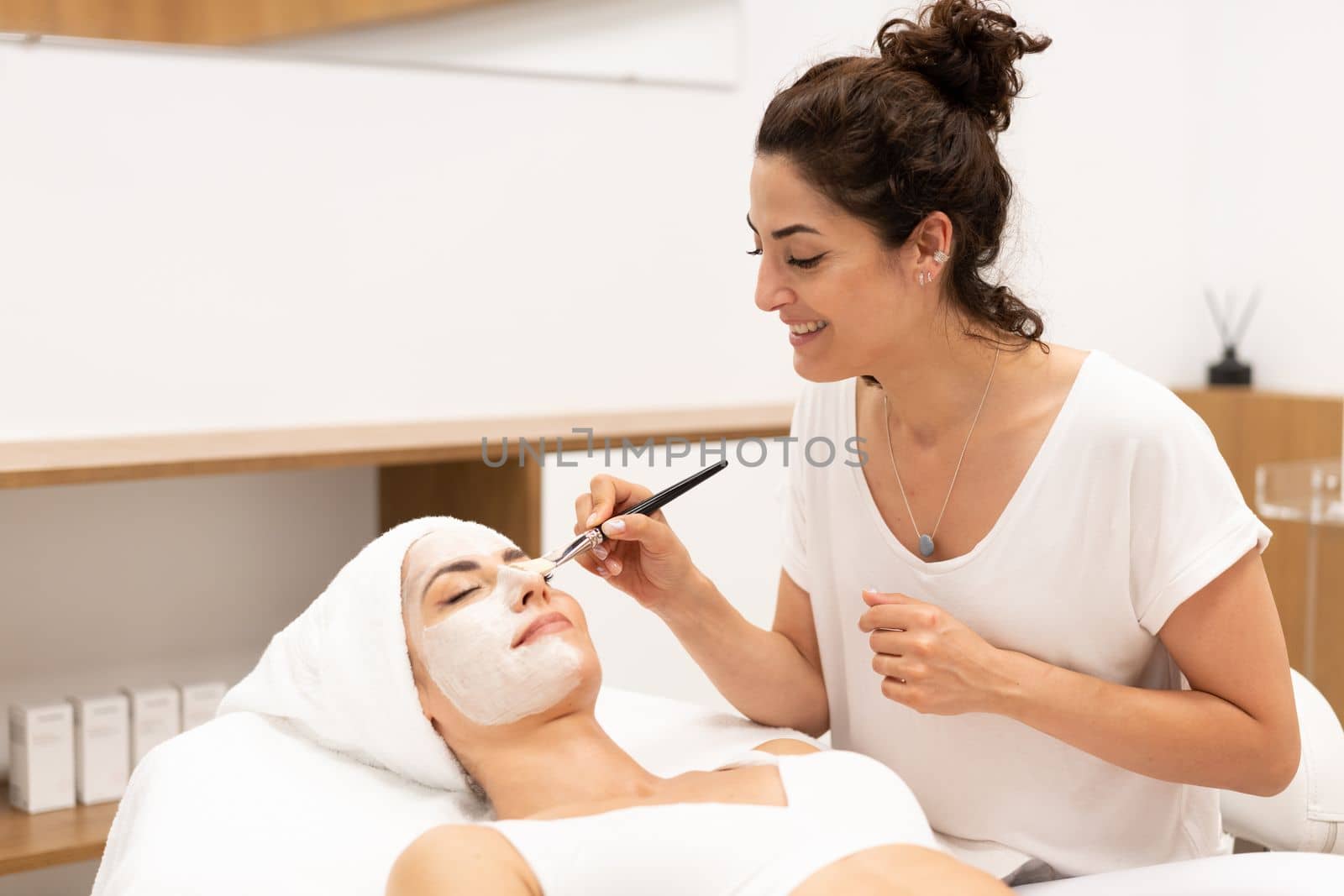 Aesthetics applying a mask to the face of a Middle-aged woman in modern wellness center. Beauty and Aesthetic concepts.