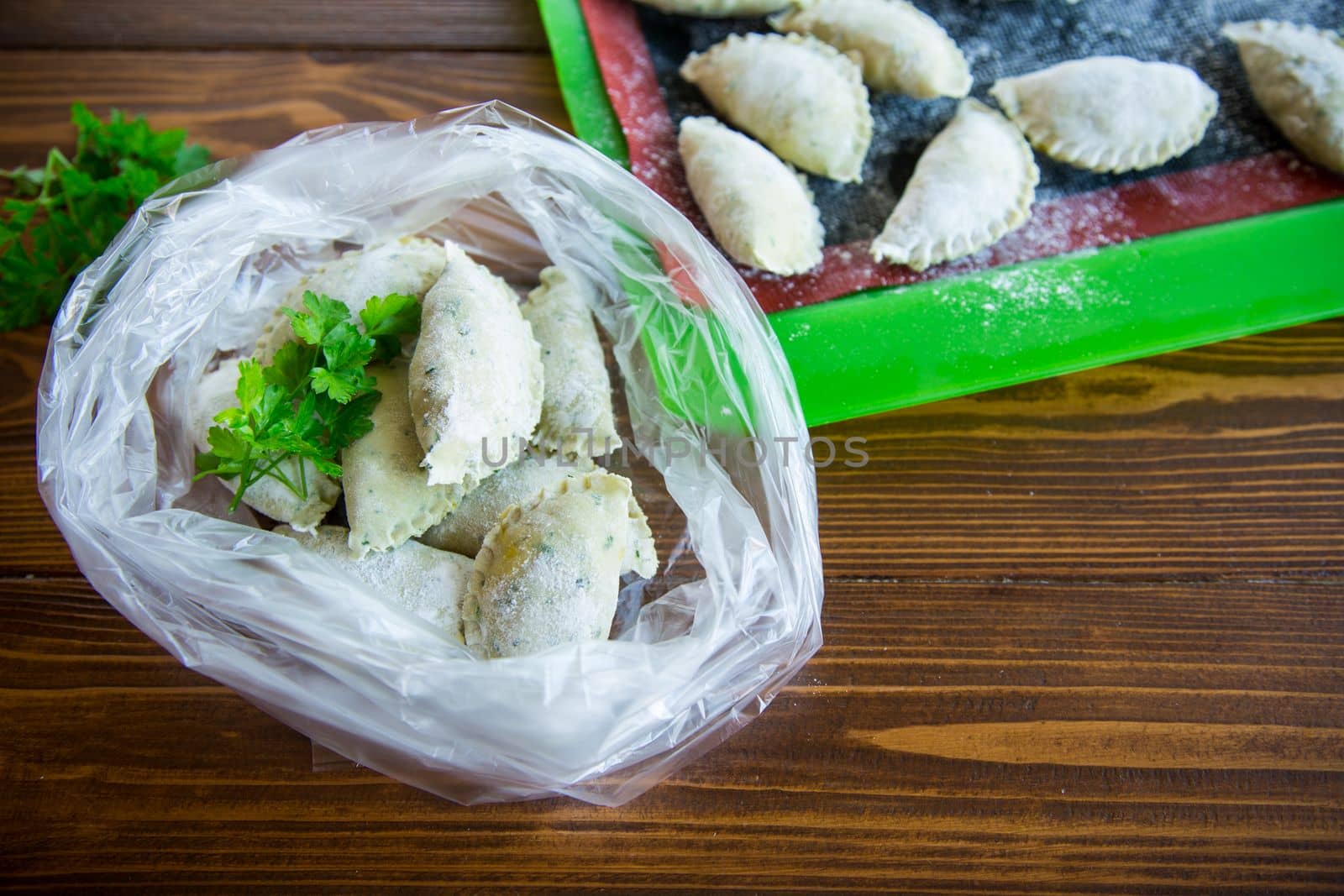 Raw green dough dumplings with parsley, dill. Raw dumplings in a bag on a wooden table.