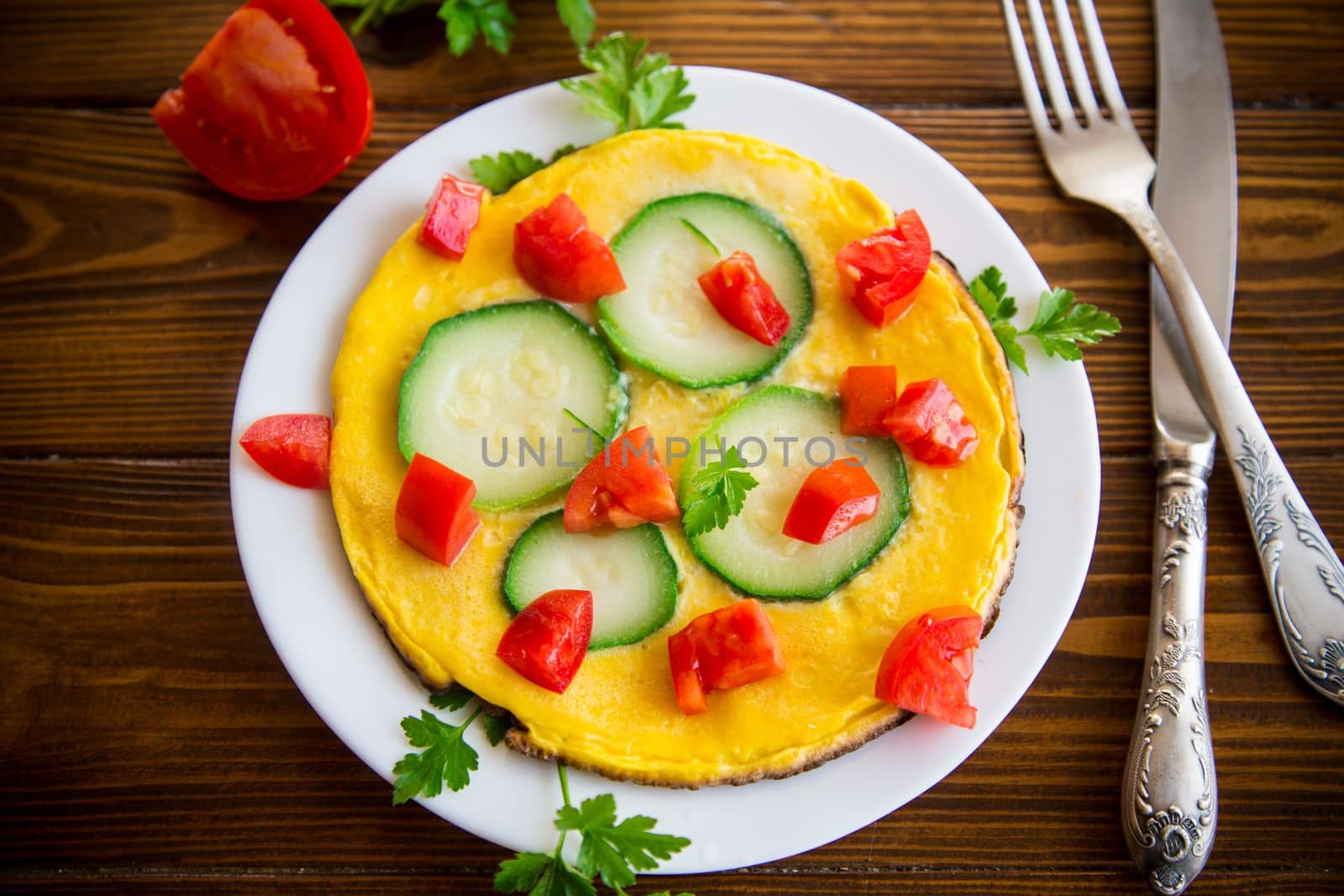 Fried omelet with zucchini, tomatoes, herbs in a plate by Rawlik
