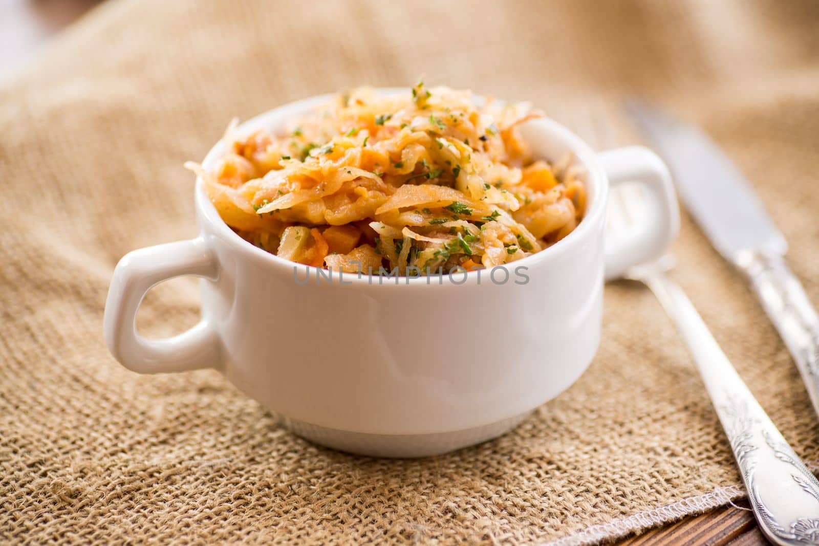 stewed cabbage with carrots and spices in a bowl on a wooden table.