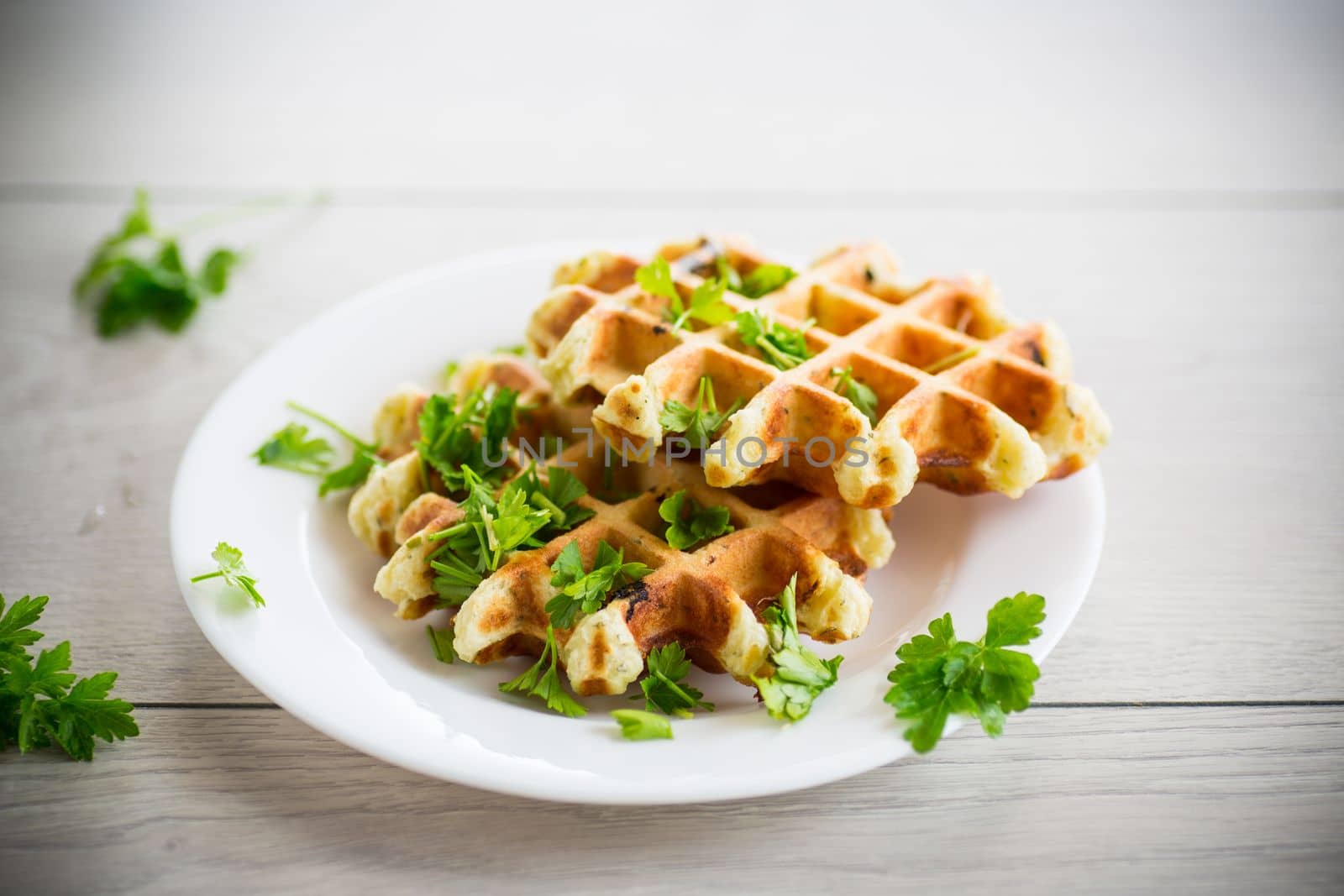 fried Belgian vegetable waffles with spices and herbs, in a plate on a light wooden table.