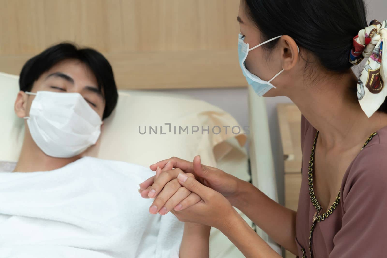 Young patient with attentive visitor and family holding hands in hospital sterile recovery room. The concept of family support for patients receiving hospital care. In-ward medical care and healthcare