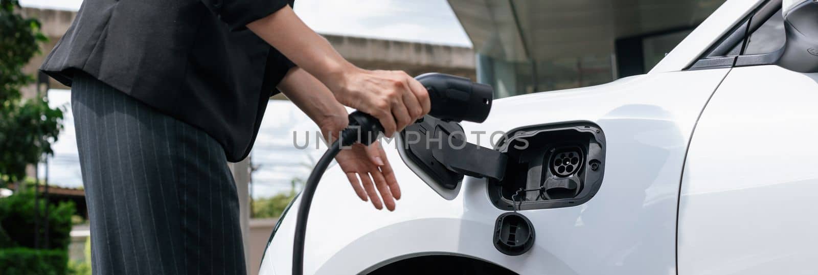 Closeup progressive businesswoman with electric vehicle at charging station. by biancoblue