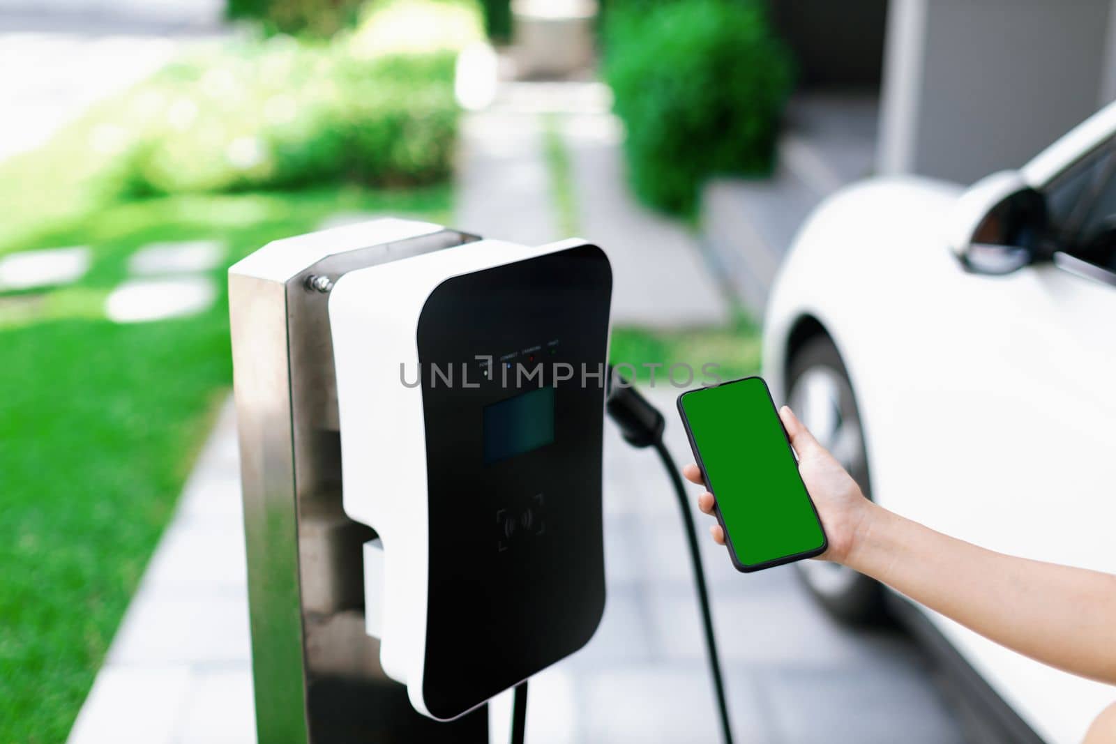 Mockup phone with green screen display energy status of electric vehicle connected to charging station for copyspace. Progressive concept for clean environment. EV powered by green renewable energy.
