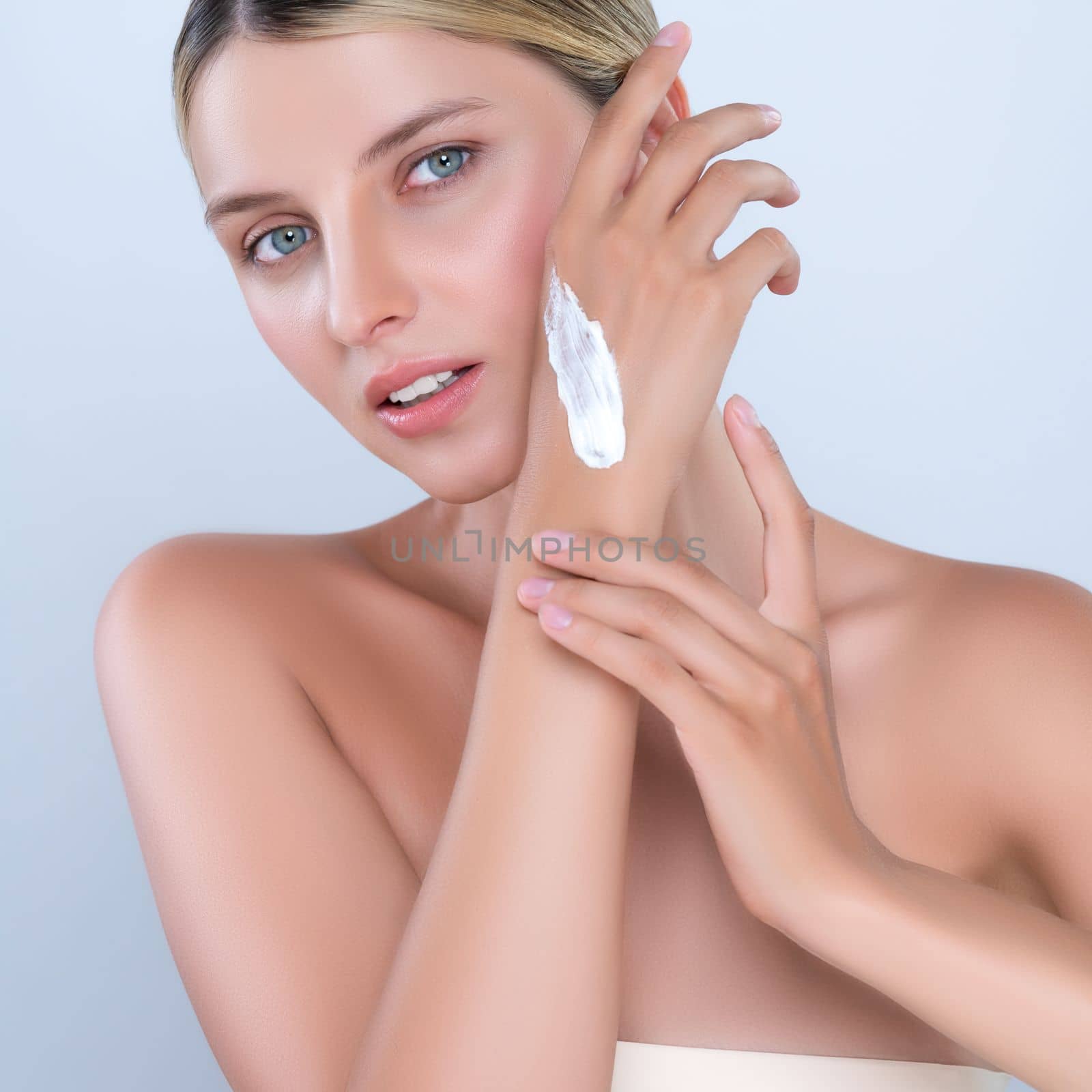 Alluring beautiful woman applying moisturizer cream on her hand for perfect skincare treatment in isolated background. Caucasian women portrait with skin rejuvenation and cosmetology concept.
