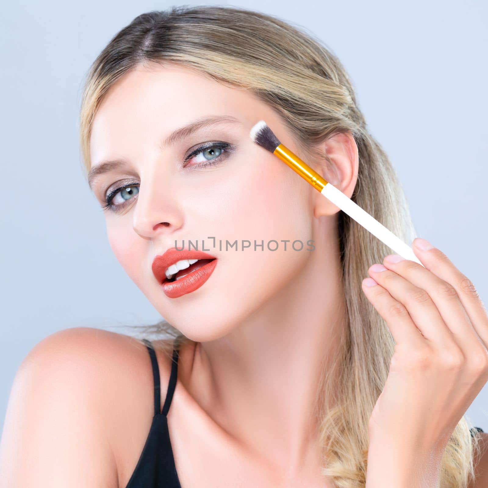 Closeup beautiful girl with flawless applying alluring eye shadow makeup with eyeliner brush. Cosmetic facial painting process on lovely young woman with perfect clean skin on isolated background.