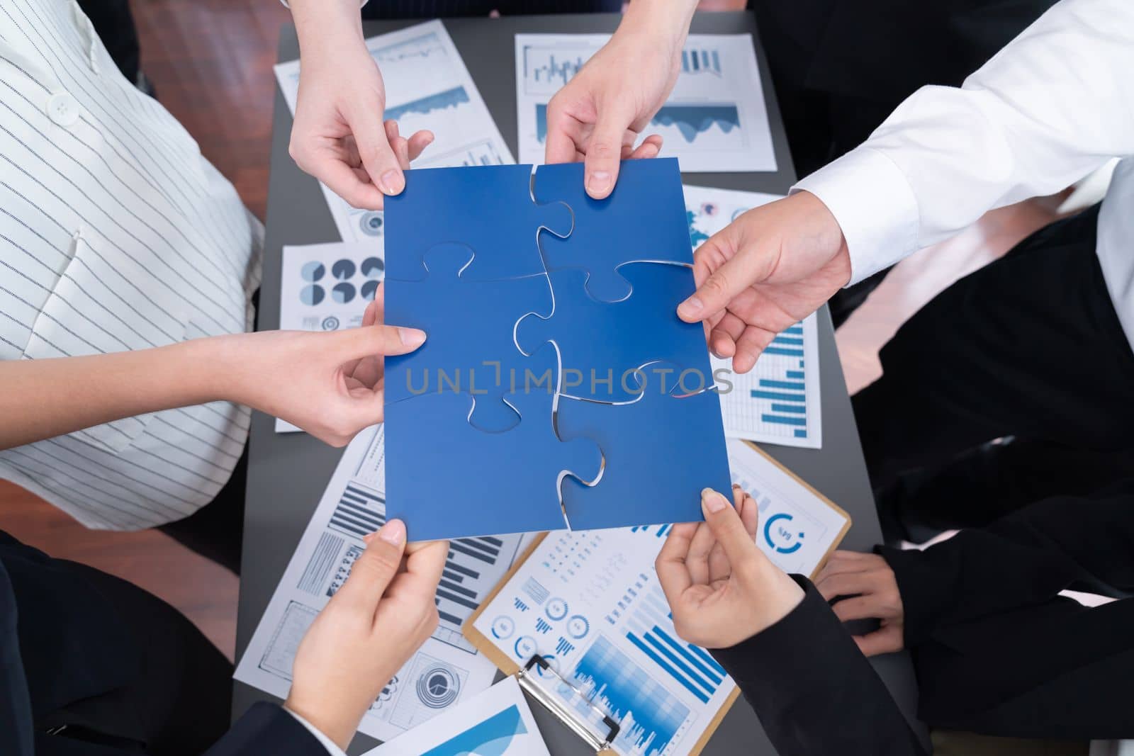 Closeup top view business team of office worker putting jigsaw puzzle together over table filled with financial report paper in workplace with manager to promote harmony concept in meeting room.